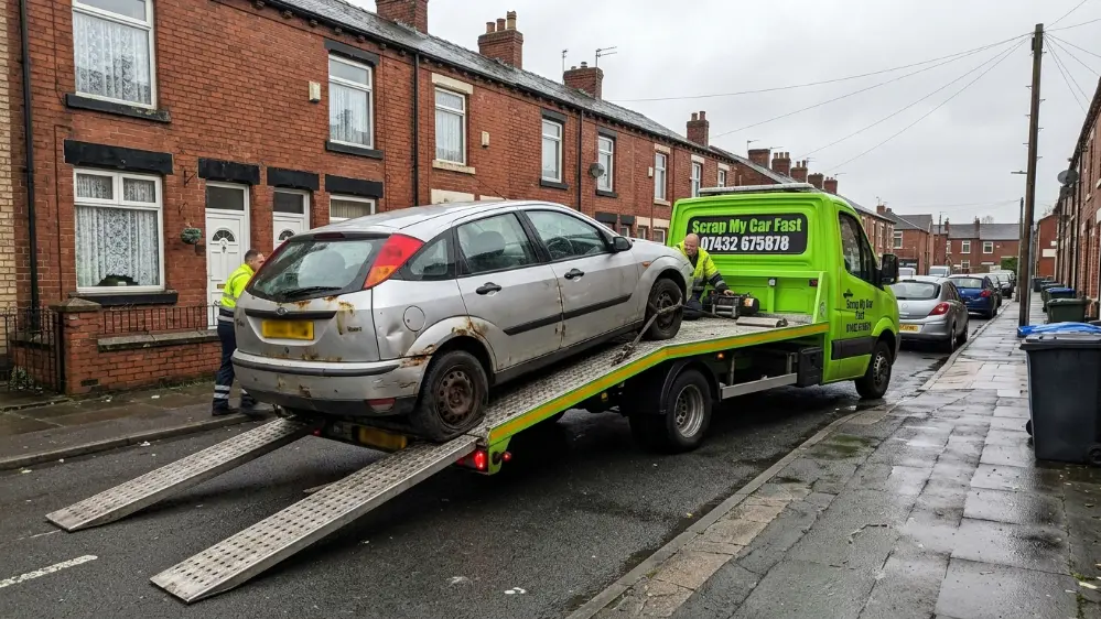 Car being loaded onto a flatbed truck for scrap collection in Bolton Greater Manchester